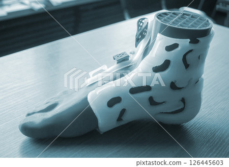 Prosthesis printed on a 3D printer from molten plastic on a plastic foot. Prototype of medical prosthesis for foot created on 3D printer. Medical orthosis, fixator, splint corset langet from plastic 126445603