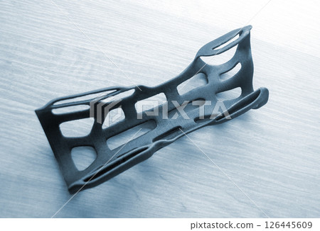 Hand splint corset prosthesis printed on 3D printer from molten black plastic powder on table. Medical orthosis fixator plastic overlay created on 3D printer. New modern medical 3D printing technology Hand splint corset prosthesis printed on 3D printer from molten black plastic powder on table. Medical orthosis fixator plastic overlay created on 3D printer. New modern medical 3D printing technology 126445609
