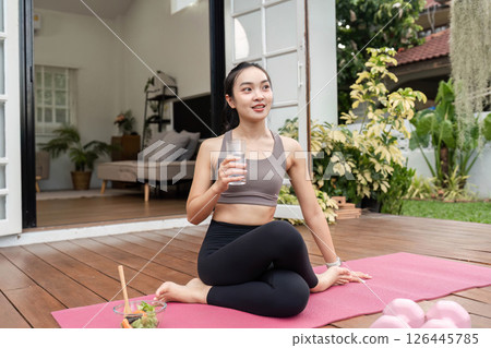 Yoga and Hydration. Young woman practicing yoga while enjoying a refreshing drink at home. 126445785