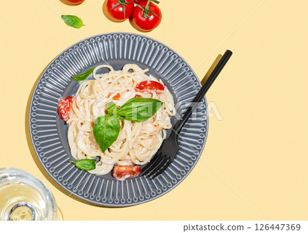 Creamy spaghetti with tomatoes, cheese and basil on a plate on a yellow background 126447369