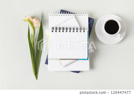 Composition with opened blank notepad, cup of black coffee, gladiolus flowers on a gray background. Festive office desktop concept. Morning coffee cup. Composition with opened blank notepad, cup of black coffee, gladiolus flowers on a gray background. Festive office desktop concept. Morning coffee cup. 126447477