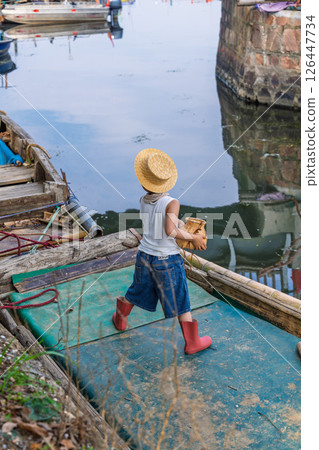 Little fisherman wearing straw hat on wooden boat near harbor 126447734