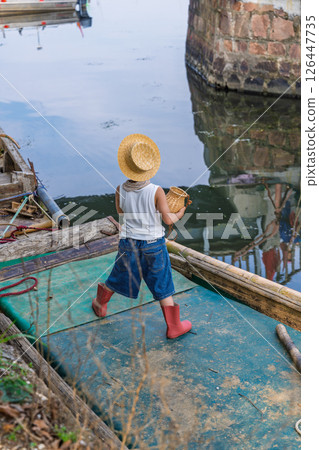 Little fisherman wearing straw hat on wooden boat near harbor Little fisherman wearing straw hat on wooden boat near harbor 126447735