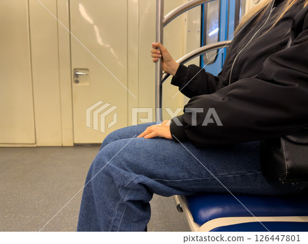 Young woman sitting in subway train during routine commute. Everyday urban transportation, practical fashion and relaxed posture while traveling through city transit system Young woman sitting in subway train during routine commute. Everyday urban transportation, practical fashion and relaxed posture while traveling through city transit system 126447801