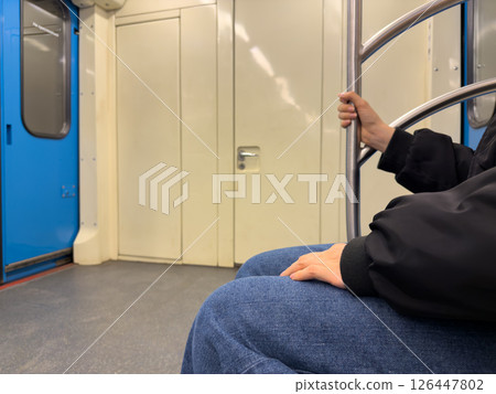 Passenger sitting inside subway train and holding handrail for safety during movement, showing importance of stable posture and cautious behavior in public transportation 126447802