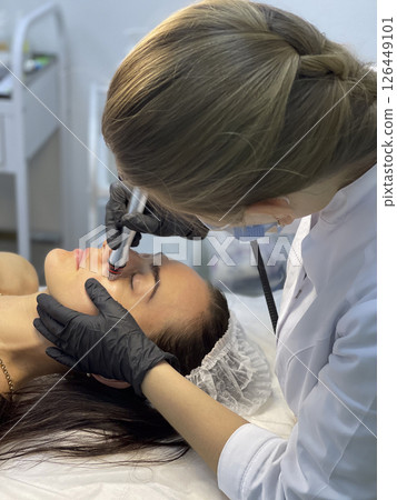 The cosmetologist in medical gloves doing a hydra peeling procedure on the client's cheeks. Side view. 126449101