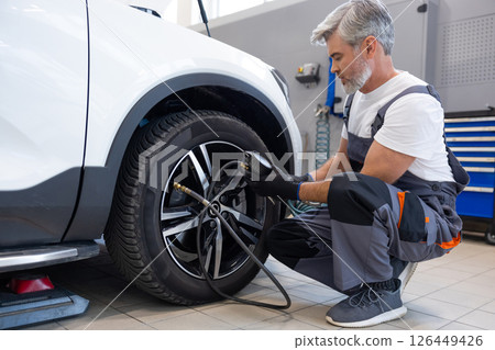 Mechanic inflating tire with pressure gauge in workshop Mechanic inflating tire with pressure gauge in workshop 126449426