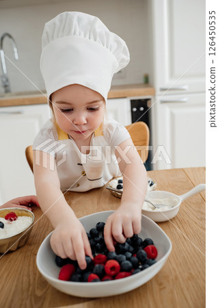 Young child enjoying a fun cooking activity by sorting fresh berries in a cozy kitchen setting 126450535