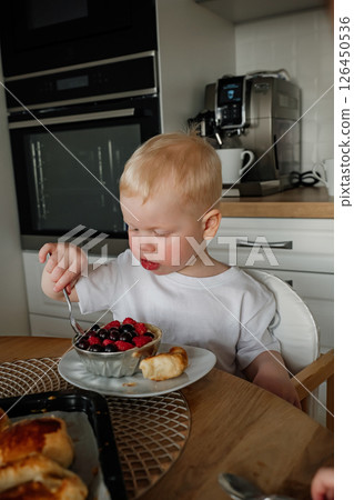 Young child enjoying a bowl of mixed berries and pastry in a modern kitchen during breakfast 126450536