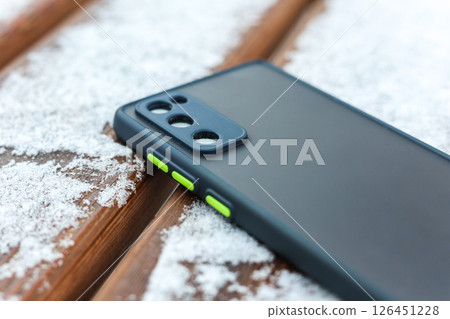 A mobile phone accidentally left on a snowy bus stop bench 126451228