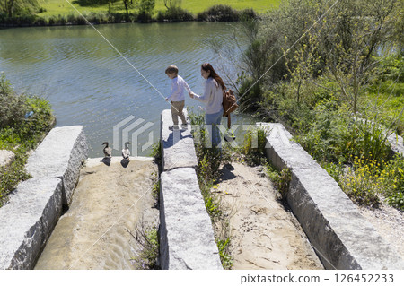 Mother and son observing ducks by the river in a sunny day 126452233