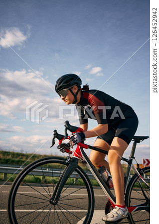 Dynamic side view photo of cyclist in aerodynamic posture gripping handlebars, highlighting bike frame, riding to finish. Dynamic side view photo of cyclist in aerodynamic posture gripping handlebars, highlighting bike frame, riding to finish. 126452942