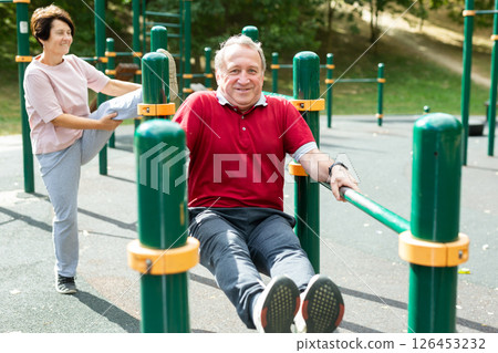 Elderly man and woman doing exercises on horizontal bars at outdoor sports ground 126453232