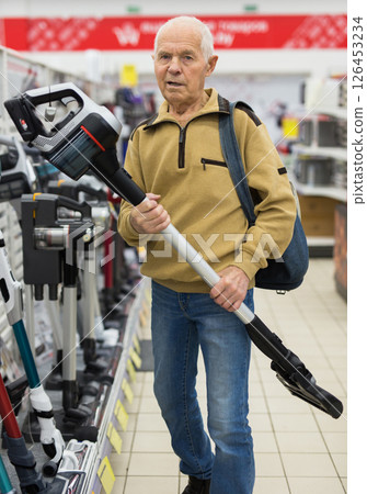 Senor man pensioner buying Upright Vacuum Cleaner in showroom of electrical appliance store Senor man pensioner buying Upright Vacuum Cleaner in showroom of electrical appliance store 126453234