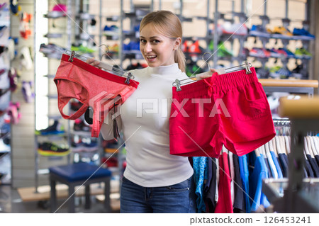 Young woman choosing summer top and shorts in clothing store 126453241