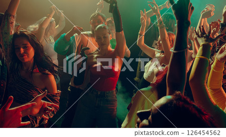 Crowd dancing energetically at a vibrant party with colorful lighting. 126454562