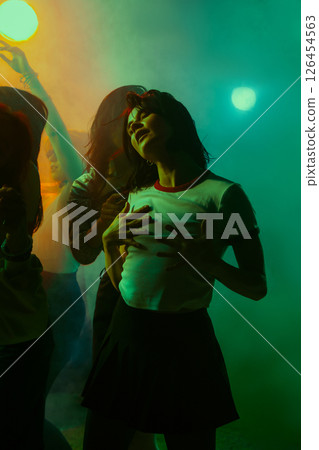 Young woman passionately dancing in vibrant, colorful lighting with a dynamic, energetic ambiance. 126454563