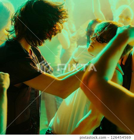 Energetic nightclub scene with people dancing in a dimly lit, smoke-filled club with vibrant green and yellow lighting 126454569