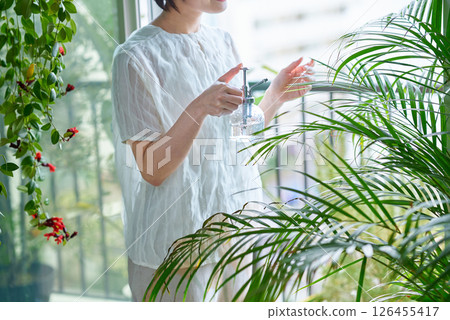 A woman watering a houseplant in a room 126455417