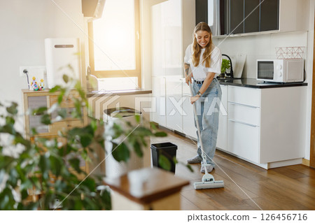 A Young Woman Busy Cleaning Her Kitchen with a Modern Mop While Enjoying Her Morning Routine A Young Woman Busy Cleaning Her Kitchen with a Modern Mop While Enjoying Her Morning Routine 126456716
