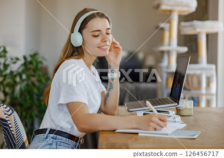 A Young Woman Engaged in Studying with Headphones On in a Cozy Home Office Environment A Young Woman Engaged in Studying with Headphones On in a Cozy Home Office Environment 126456717