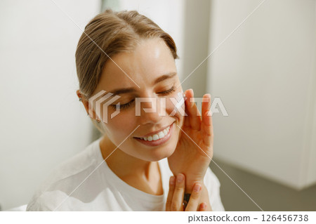 A Smiling Woman is Happily Enjoying Her Skincare Routine While at Home, Feeling Radiant 126456738