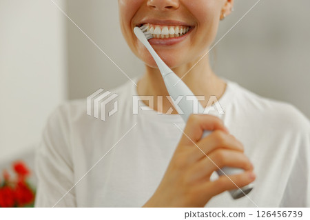 A Bright Smile A Woman Brushing Her Teeth with an Electric Toothbrush in the Bathroom 126456739