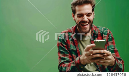 Happy man smiling at smartphone while sitting in front of green background during the day 126457056