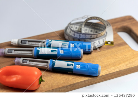 Ozempic Insulin injection pen for diabetics and weight loss and a cutting board with vegetables and a measuring tape. Ozempic Insulin injection pen for diabetics and weight loss and a cutting board with vegetables and a measuring tape. 126457290