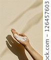 A hand holding a creamy skincare product against a soft beige background with gentle shadows in natural light 126457603