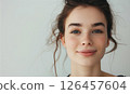 A young woman smiling gently with soft features and loose hair against a light background in a serene indoor setting 126457604