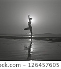 A silhouetted figure practices yoga on a serene beach at sunset, creating a peaceful atmosphere with reflections on the water 126457605