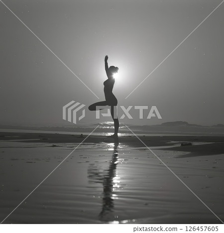 A silhouetted figure practices yoga on a serene beach at sunset, creating a peaceful atmosphere with reflections on the water 126457605