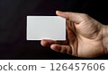 A person holding a blank card with one hand against a dark background in a minimalist setting for emphasis on simplicity and focus 126457606