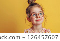 Young girl with glasses smiling against a bright yellow background, showcasing her playful spirit and innocence 126457607