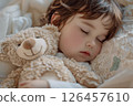 A peaceful toddler sleeping soundly with a stuffed bear in a cozy, softly lit bedroom setting during a serene morning 126457610