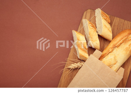 Baguette whole and cut into pieces on cutting board on brown background Baguette whole and cut into pieces on cutting board on brown background 126457787