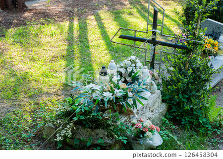 Serene Catholic cemetery with rustic iron cross and lush floral tributes in peaceful sunlit setting featuring greenery and floral arrangements Serene Catholic cemetery with rustic iron cross and lush floral tributes in peaceful sunlit setting featuring greenery and floral arrangements 126458304