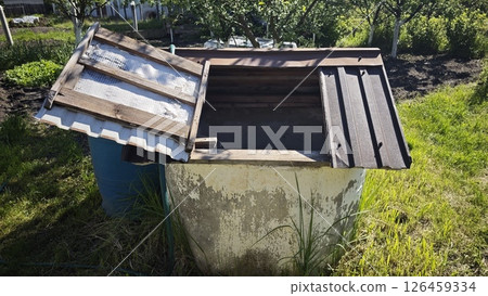Old concrete well with a wooden lid standing on green grass in a sunny countryside garden. Concept of traditional water source and rural sustainability 126459334