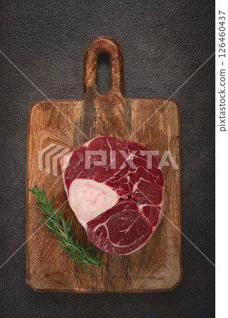a shank on the bone, raw meat for ossobuco, on a wooden chopping board, with a branch of rosemary, top view, no people. a shank on the bone, raw meat for ossobuco, on a wooden chopping board, with a branch of rosemary, top view, no people. 126460437