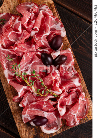Freshly cut dried meat, served with olives and herbs, on a wooden chopping board, no people, 126460462