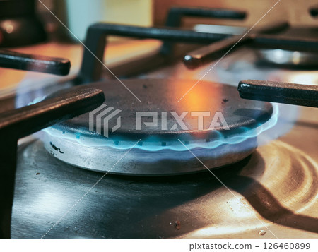 Blue flames flickering across gas stove burner, generating cooking heat in modern kitchen, representing culinary intensity Blue flames flickering across gas stove burner, generating cooking heat in modern kitchen, representing culinary intensity 126460899