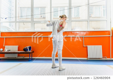 Female fencer putting on protective gear before match indoors. 126460904