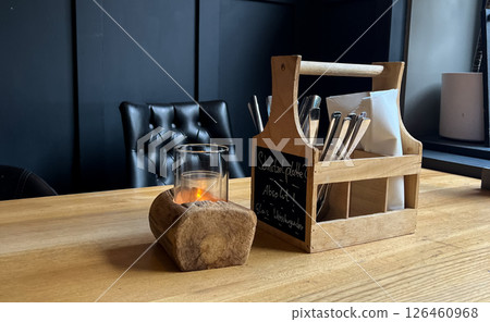 A wooden table with a rustic utensil holder and a glass candle holder. The setting is modern and cozy,  126460968