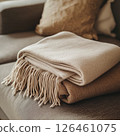 A soft, natural light highlights a knitted blanket mockup neatly folded on a plush couch, evoking a homely atmosphere with its warm tones and gentle focus. 126461075