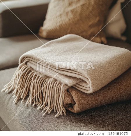 A soft, natural light highlights a knitted blanket mockup neatly folded on a plush couch, evoking a homely atmosphere with its warm tones and gentle focus. 126461075