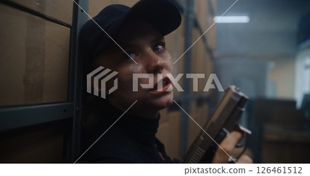Close Up of Female Secret Agent Hiding Behind Cover in Warehouse, Holding a Pistol, Talking to Killer 126461512