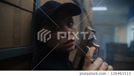 Close Up of Female Secret Agent Hiding Behind Cover in Warehouse, Holding a Pistol, Talking to Killer 126461513