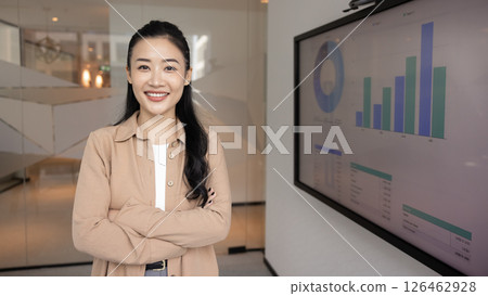 Marketing analyst standing in office next to screen displaying data 126462928