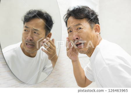 A man looking in the mirror and worrying about his hair and skin A man looking in the mirror and worrying about his hair and skin 126463965